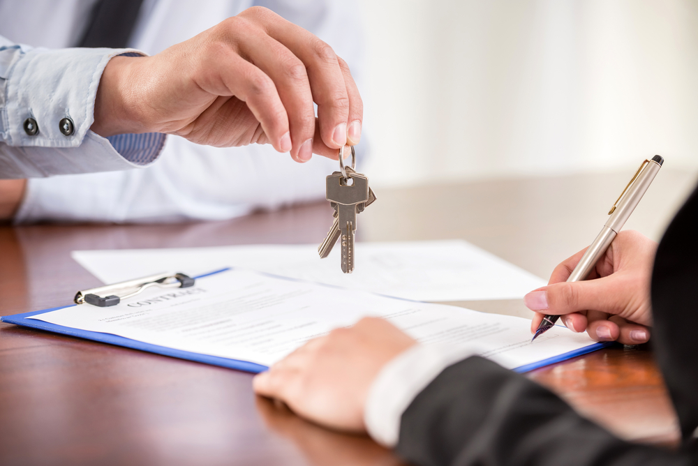 A man handing keys to someone while signing a document illustrating the need to find realtors near me